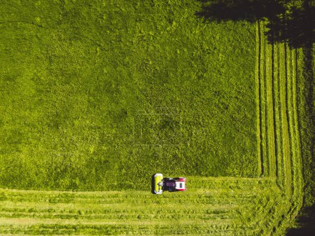 Téléchargez les photos : Aerial view of a tractor mowing a green fresh grass field, a farmer in a modern tractor mowing a green fresh grass field on a sunny day. High quality photo - en image libre de droit