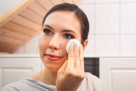 Photo for Beautiful young woman cleaning her face, removing make up with a cotton pad and micellar water. Skin care and beauty. Young beautiful woman cleaning her face. High quality photo - Royalty Free Image