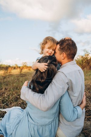 Téléchargez les photos : Jeune couple avec mignon sourire fille de deux ans embrassant maman et papa en tenue bleu clair - en image libre de droit