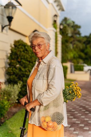 Téléchargez les photos : Femmes âgées tenant des fleurs jaunes et souriant en robe orange - en image libre de droit