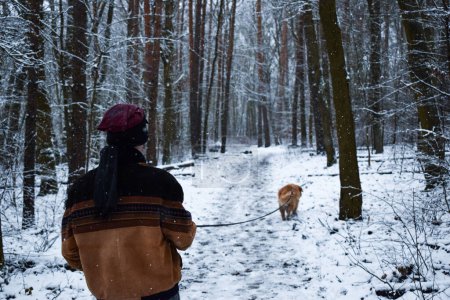 Foto de Masculino con su perro en una correa caminando sobre un bosque de pinos nevados en invierno - Imagen libre de derechos
