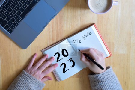 Photo for Young woman hand writing in a 2023 new year notebook with list of resolutions while drinking a vegan coffee milk - Royalty Free Image