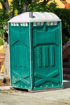 Photo for Green outhouse in urban area of city for workers to use restroom during construction projects of city infrastructure. Factory usage with white roof on concreate for laborers to utelize downtown. - Royalty Free Image
