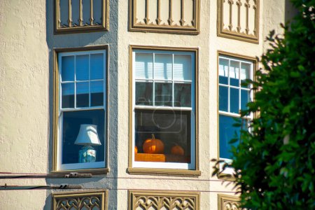 Photo for Beige cement building with bay windows with white accent frames and decorative facade with lamps and pumpkins inside. Donwotnw urban neighborhood with front yard trees and loft apartment. - Royalty Free Image