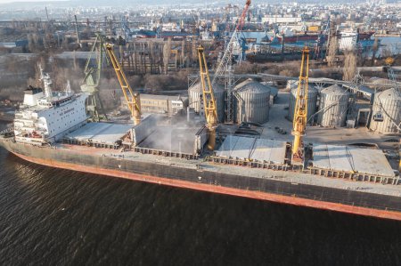 Photo for Aerial drone shot grain deal 2023. Close up Bunkering of dry cargo ship with grain at sunset golden hour. Loading with harbor crane - Royalty Free Image