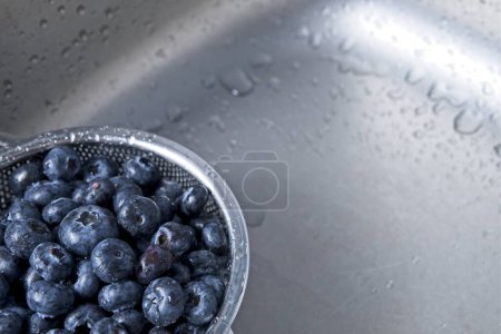 Téléchargez les photos : Bleuets fraîchement lavés dans une passoire en acier inoxydable dans un évier de cuisine, gros plan - en image libre de droit