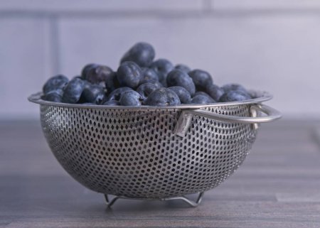 Téléchargez les photos : Gros plan de bleuets fraîchement lavés dans une passoire en acier inoxydable sur un comptoir de cuisine - en image libre de droit