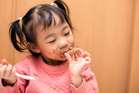 Foto de A toddler child eating chocolate ice cream in a cone with a messy face - Imagen libre de derechos