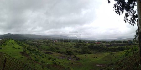 Photo for Panoramic landscape view of wide open lush green grassland against mountains on a cloudy monsoon day. Clicked near Pawna or Pavana lake in Lonavala, a famous tourist place in Pune, Maharashtra, India - Royalty Free Image