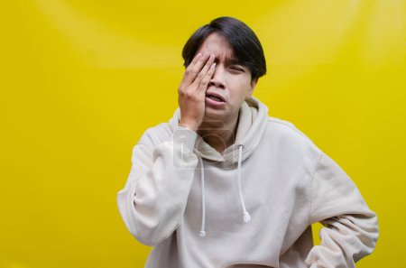 Photo for Sad A young Asian man crying face expression with hands gesture is isolated over a yellow background - Royalty Free Image