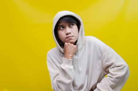 Photo for Thoughtful, confused Asian man thinking and wondering whether to choose something isolated on a yellow background - Royalty Free Image