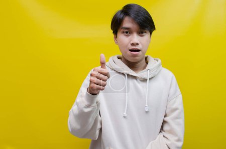 Téléchargez les photos : Pour les concepts de publicité et de placement de produits, un jeune Asiatique heureux et souriant ouvre les paumes et pointe vers l'espace de copie - en image libre de droit