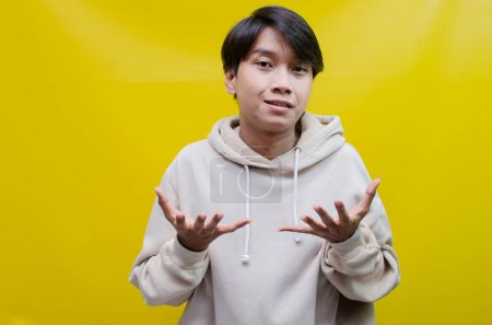 Photo for For advertising and product placement concepts, a happy, smiling young Asian man opens his palms and points to copy space - Royalty Free Image