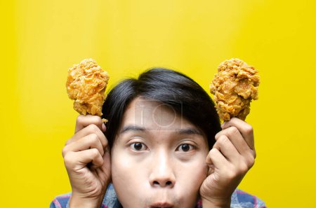 Téléchargez les photos : Drôle expressif asiatique homme tient poulet frit avec wow expression isolé sur fond jaune. concept d'aliments malsains - en image libre de droit