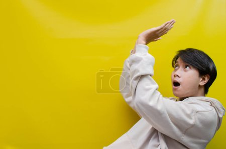 Foto de Vista lateral del hombre asiático en una sudadera con capucha beige señalando sus dedos y abriendo los brazos para promover y anunciar algo bueno. - Imagen libre de derechos