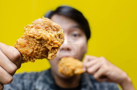 Téléchargez les photos : Focus sélectif sur les mains de l'homme tenant du poulet frit avec une expression visage surprise sur fond jaune - en image libre de droit