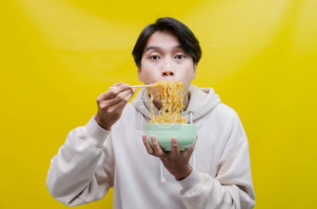 Foto de Hombre asiático oliendo y disfrutando con placer deliciosos fideos. un hombre da deliciosas expresiones mientras come fideos. - Imagen libre de derechos