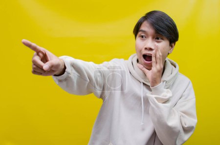 Téléchargez les photos : Asiatique homme portant un beige sweat à capuche crier et chuchoter pour annoncer de bonnes nouvelles. - en image libre de droit