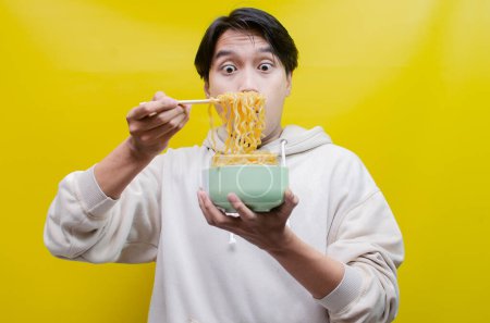 Téléchargez les photos : Homme asiatique sentant et appréciant avec plaisir de délicieuses nouilles. un homme donne de délicieuses expressions tout en mangeant des nouilles. - en image libre de droit