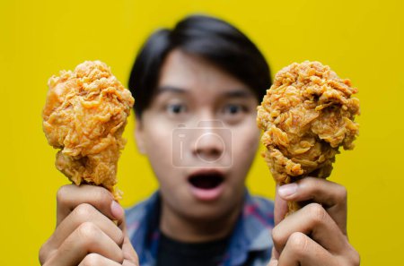 Photo for Selective focus on man's hands holding fried chicken with surprised face expression on yellow background - Royalty Free Image