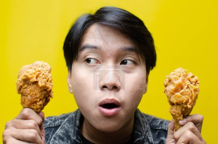 Foto de Hambriento hombre sostiene frito muslo pollo aislado sobre amarillo fondo - Imagen libre de derechos