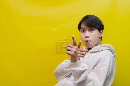 Photo for Asian man in beige hoodie dancing happily and raising his fist celebrating victory on yellow background - Royalty Free Image