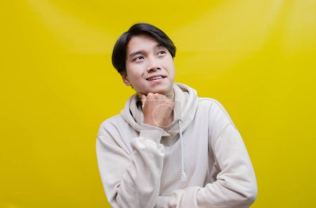 Photo for A thoughtful, confused Asian man thinking and wondering whether to choose something isolated on a yellow background - Royalty Free Image