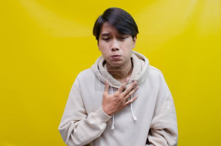Téléchargez les photos : Triste Un jeune homme asiatique pleurant expression du visage avec des mains geste est isolé sur un fond jaune - en image libre de droit