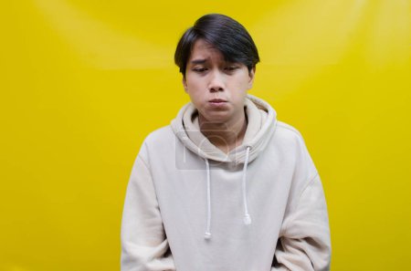 Téléchargez les photos : Triste Un jeune homme asiatique pleurant expression du visage avec des mains geste est isolé sur un fond jaune - en image libre de droit