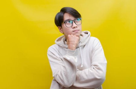 Foto de Un hombre asiático pensativo y confuso pensando y preguntándose si elegir algo aislado sobre un fondo amarillo - Imagen libre de derechos