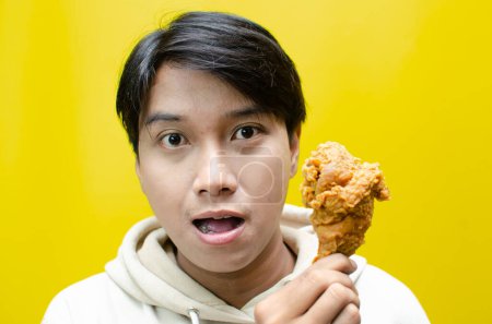 Photo for Happy surprised asian man holds fried chicken with wow expression isolated over yellow background. unhealthy food concept. food sale promotion - Royalty Free Image