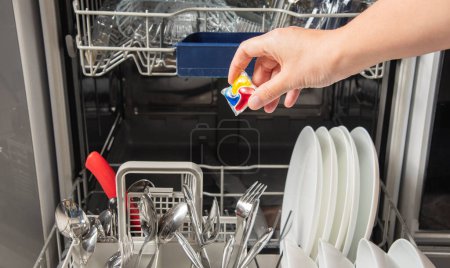 Woman putting detergen tablet into open dishwasher. Household, housekeeping, domestic concept