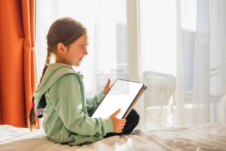 Téléchargez les photos : European Little Girl with Tablet pc Relaxing in a spacious room near the Window - en image libre de droit