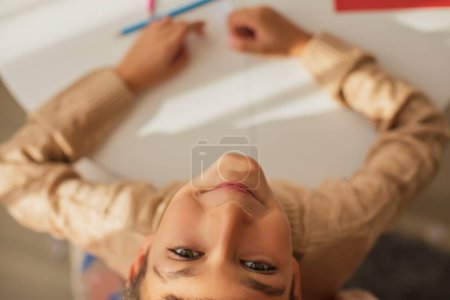 Téléchargez les photos : Child boy painting with colored pencils and making crafts and cardboard and colored paper uses glue and scissors - en image libre de droit