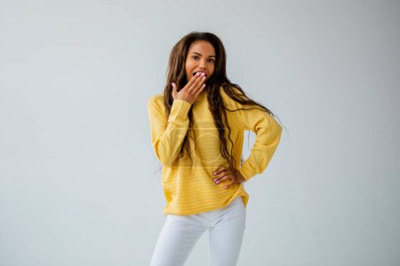 Photo for Portrait of a cute black woman in a yellow sweater posing in the studio on a white wall, natural ligh - Royalty Free Image