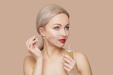 Foto de Portrait of a woman with natural makeup, model applying moisturizing fluid with gold particles, red lips, perfect fresh and healthy skin. - Imagen libre de derechos
