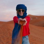 General view of a woman with a Berber scarf dropping sand from her hands from the top of a dune in the Sahara desert. High quality photo