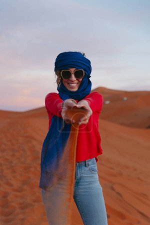 Photo for General view of a woman with a Berber scarf dropping sand from her hands from the top of a dune in the Sahara desert. High quality photo - Royalty Free Image