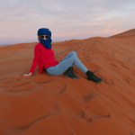 Young girl sitting on top of a dune in the sahara at sunset with a berber scarf. High quality photo
