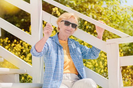 Foto de Mature attractive woman traveler sitting alone on the terrace of beach coffee shop in Bulgaria and waving to acquaintances. Active life of the elderly in retirement - Imagen libre de derechos