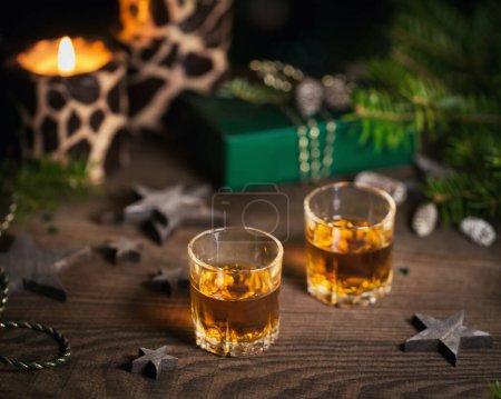 Foto de Two glasses of whiskey or bourbon with Christmas decoration on dark background. New Year, Christmas and winter holidays whiskey mood concept - Imagen libre de derechos