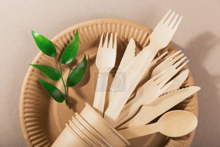 Foto de Utensilios desechables ecológicos hechos de madera de bambú y papel sobre un fondo beige claro. Tenedor, cuchillos, platos, vasos de papel y pajitas - Imagen libre de derechos