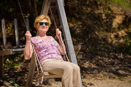 Téléchargez les photos : Femme âgée se balançant joyeusement sur une balançoire et ayant ventilateur. Bon concept de retraite - en image libre de droit