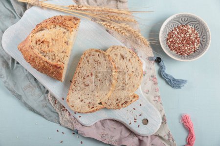 Téléchargez les photos : Trancher le pain de grains entiers frais cuit au four avec des graines de lin et des graines de sésame sur un carton bleu clair. Boulangerie - en image libre de droit