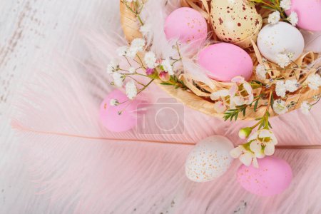 Téléchargez les photos : Easter candy chocolate eggs and almond sweets lying in a birds nest decorated with flowers and feathers on white wooden background. Happy Easter concept. - en image libre de droit