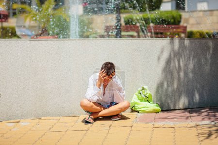 Trauriger depressiver Teenager, der aufgebracht in der Nähe des Brunnens sitzt und seinen Kopf in den Händen hält. Die Idee, Kinder und die psychische Gesundheit von Kindern zu schützen