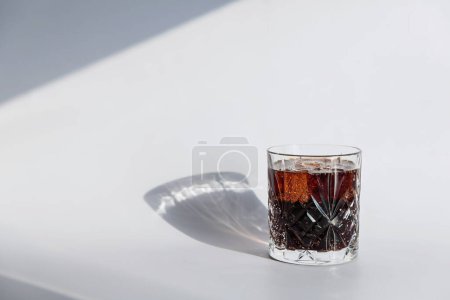 Whiskey cola cocktail with strong alcohol and ice in highball glass on white background with hard light
