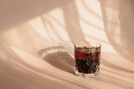 Photo for Whiskey cola cocktail with strong alcohol and ice in highball glass on light beige background with shadows and fantastic highlights and reflecting bright sunlight in daytime - Royalty Free Image