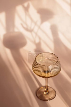 Dos copas con vino blanco colocadas sobre fondo beige claro con sombras y fantásticos reflejos y reflejando la brillante luz del sol durante el día