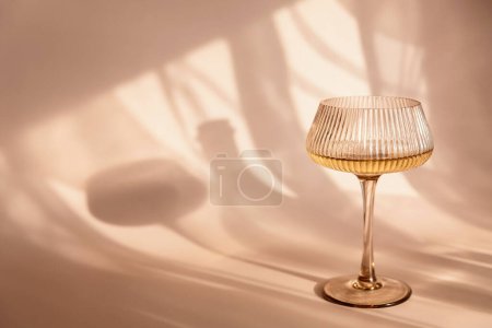 Dos copas con vino blanco colocadas sobre fondo beige claro con sombras y fantásticos reflejos y reflejando la brillante luz del sol durante el día